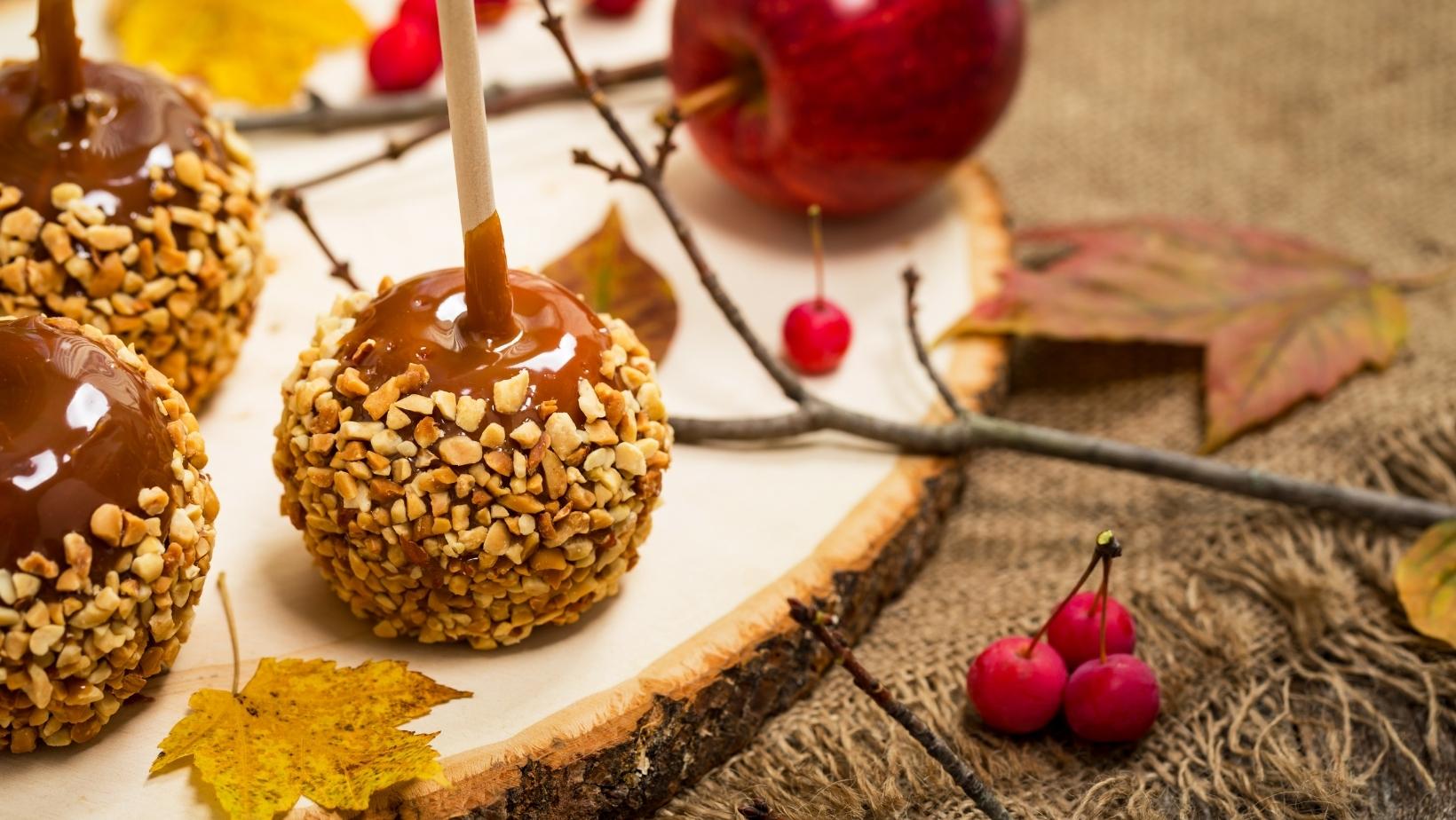 Caramel apples with nuts on a wooden cutting board on a table with fall berries and twigs